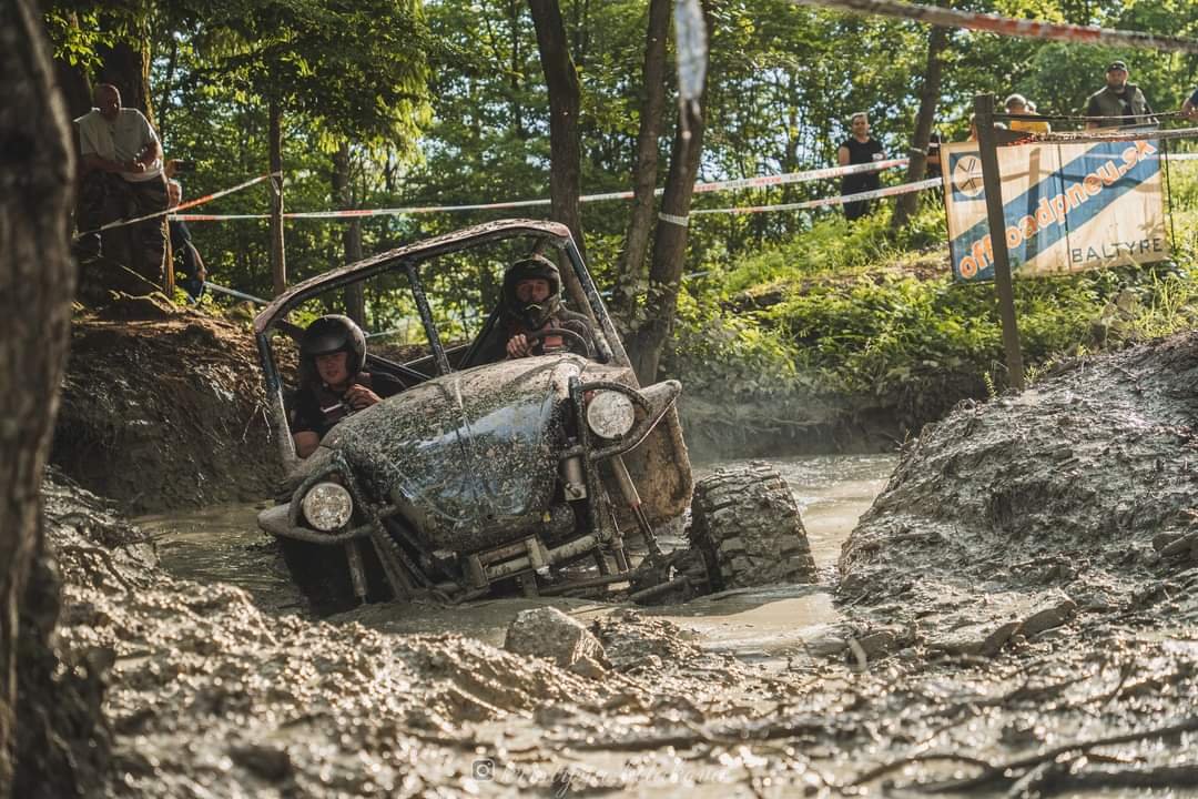 Terénne vozidlo v blate počas off-road súťaže s dvoma vodičmi v prilbách